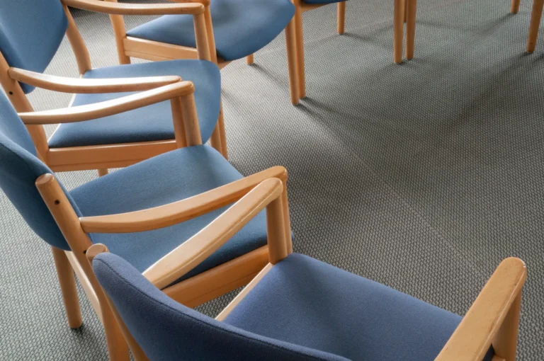 Prázdné modré židle v terapeutické místnosti připravené pro skupinové sezení v Praze.